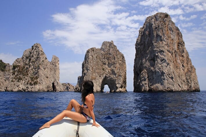 Woman sitting on a boat in front of the Faraglioni Rocks in Capri Italy