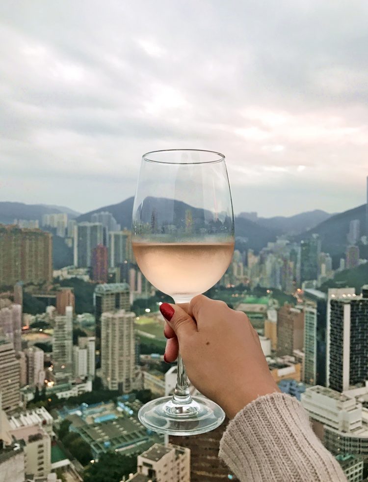 Woman's hand holding wine glass with view over Happy Valley in Hong Kong