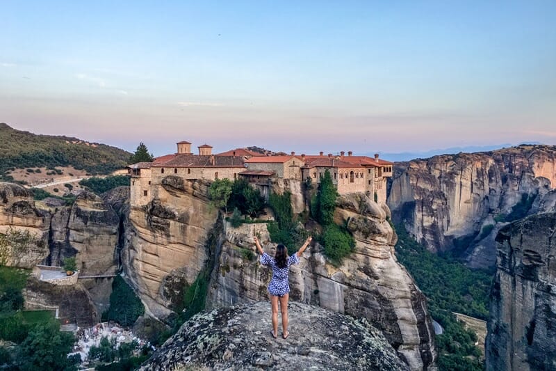 Woman standing in front of a hanging monastery in Meteora Greece